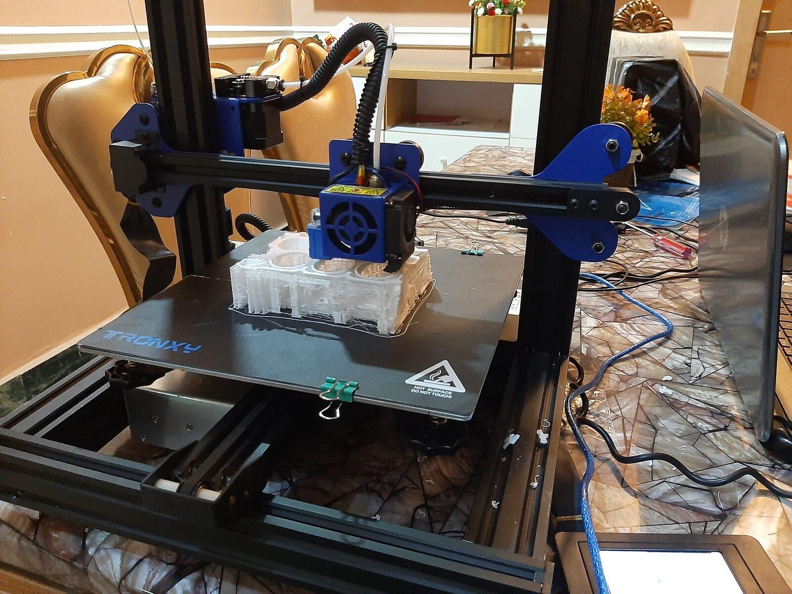 The assembled 3D printer mid-print, with a miniature engine block taking shape on the bed